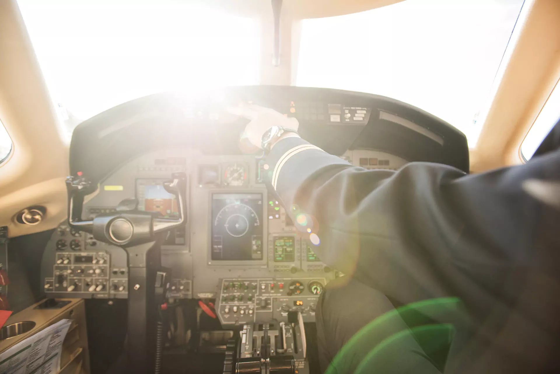 Pilot adjusting controls in a sunlit aircraft cockpit.